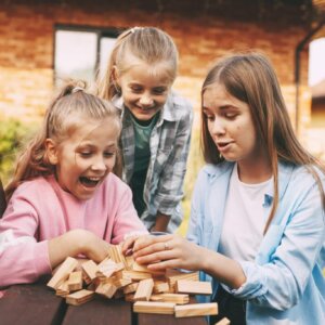Three girlfriends play a wooden board game outdoors near their house. Children's leisure and development concept.